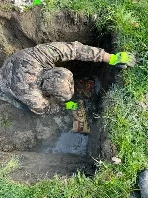 Worker in safety gear excavating underground drain pipe for inspection and repair
