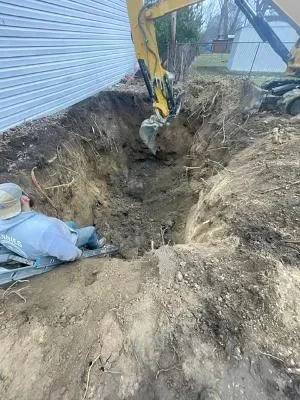 Excavator digging deep trench for underground utility installation with exposed soil layers