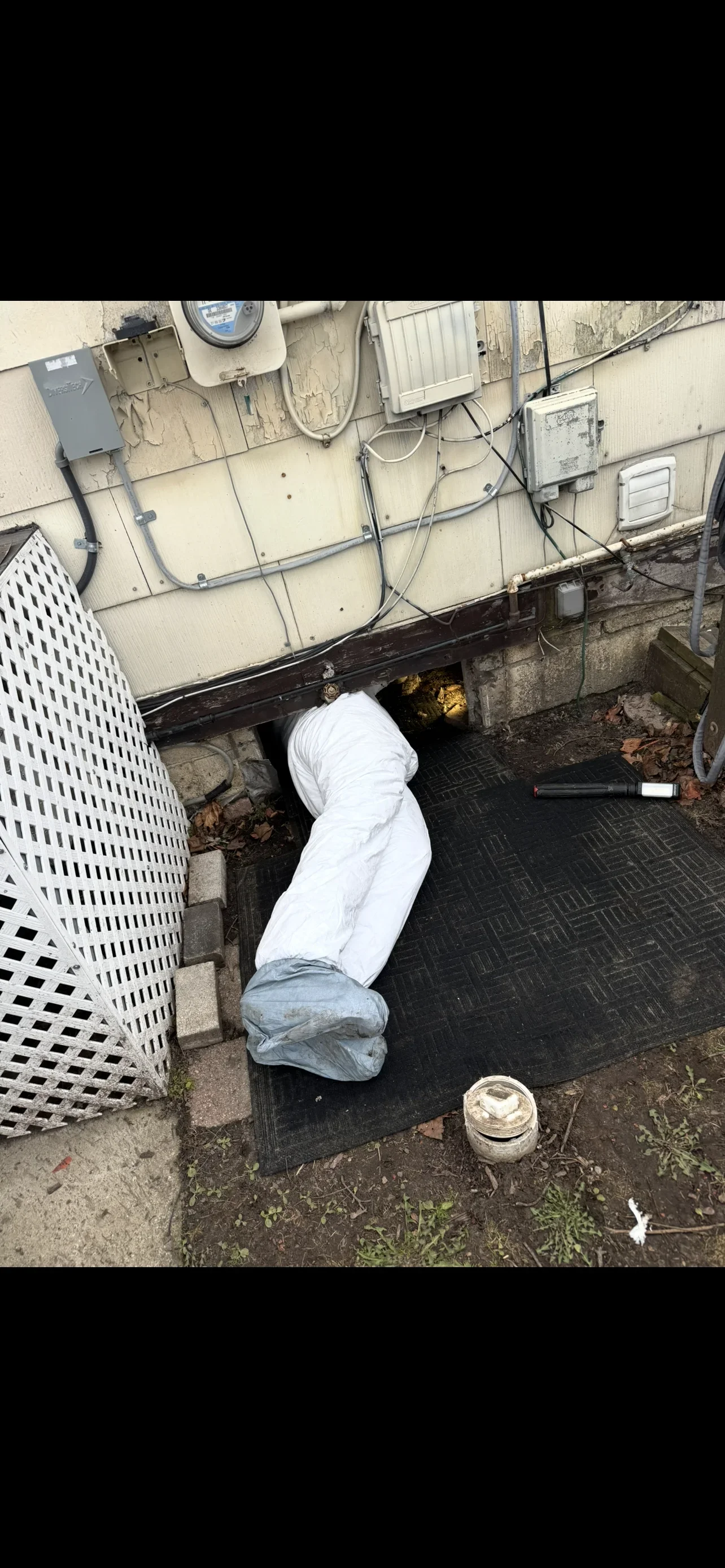 Technician working in excavated basement drain pit with white protective covering and black drainage mat