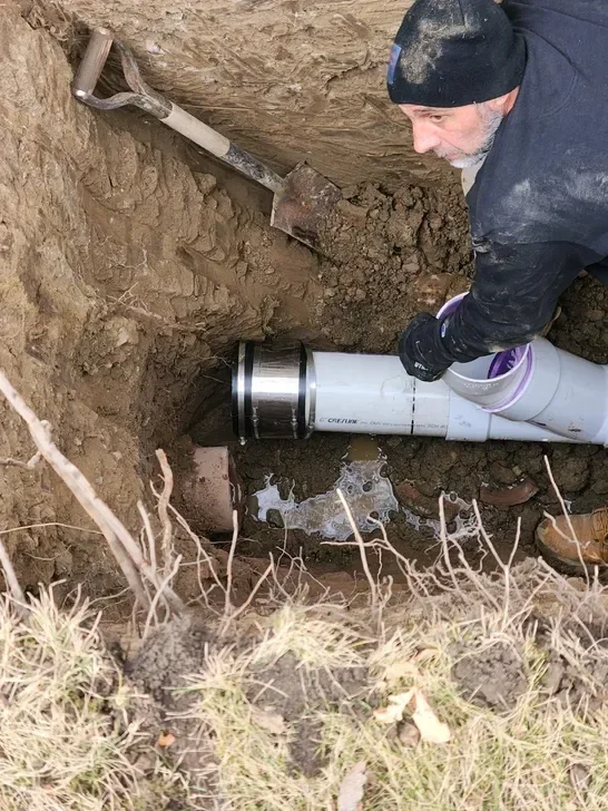 Technician installing white PVC drain pipe in underground trench with soil excavation