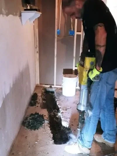 Excavated drain line showing damaged pipe and soil infiltration beneath residential foundation