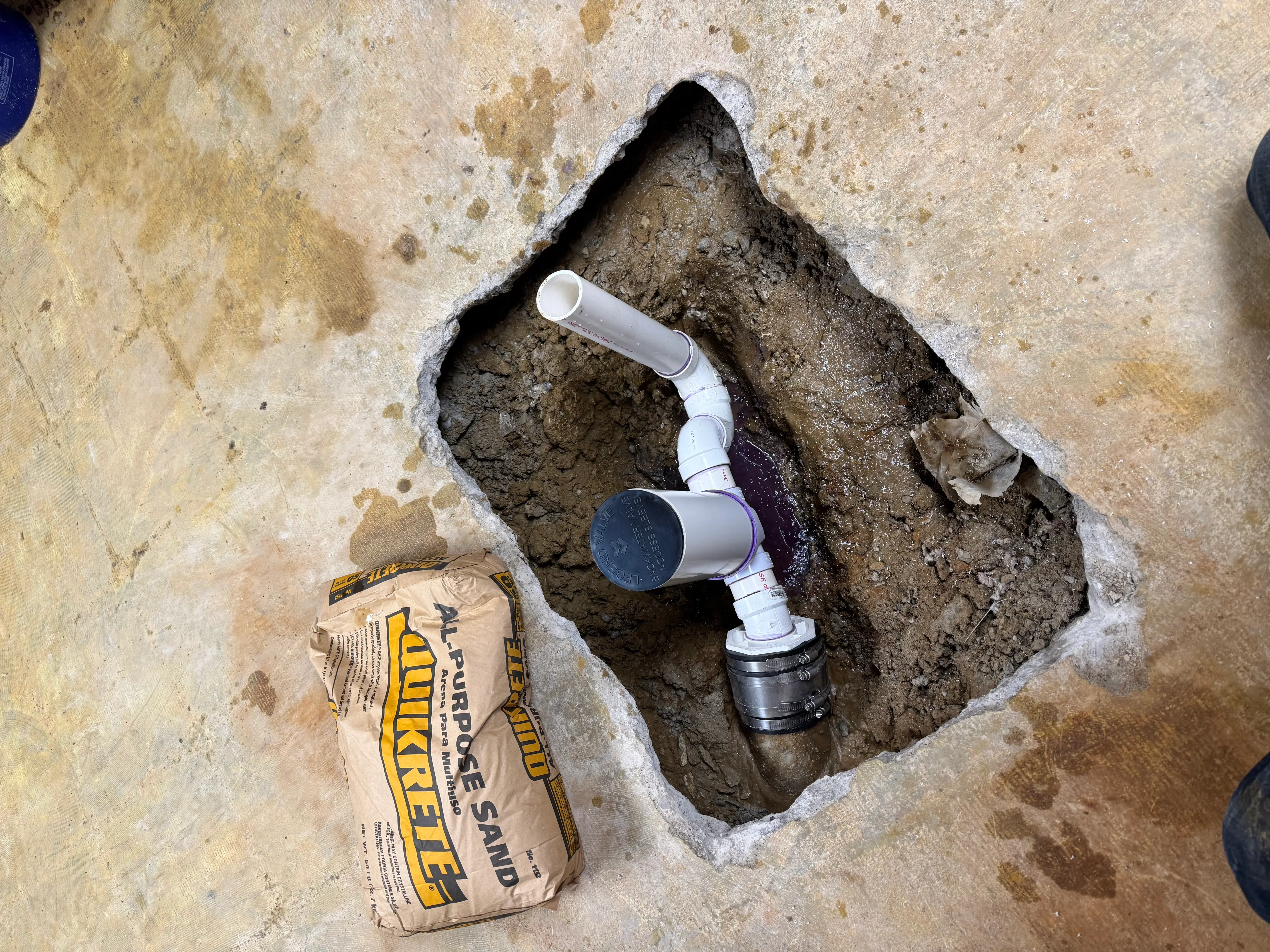 White PVC drain pipe with elbow fittings installed in underground excavation with concrete collar