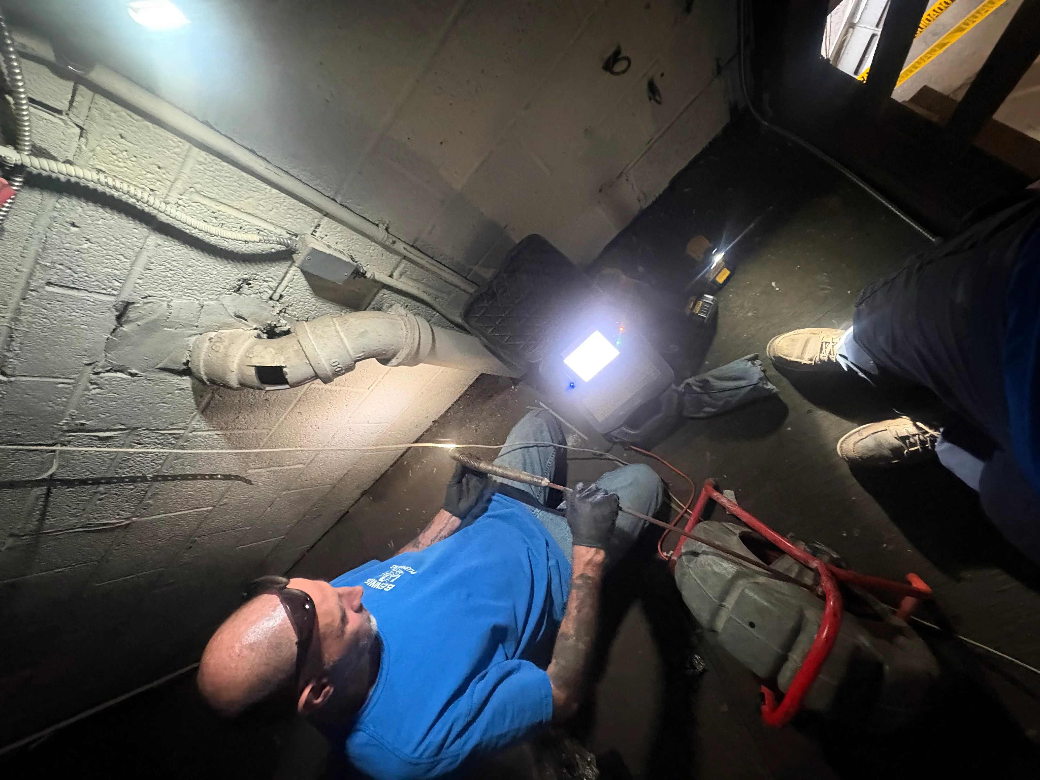 Plumber inspecting cast iron and PVC drain lines in basement using work light