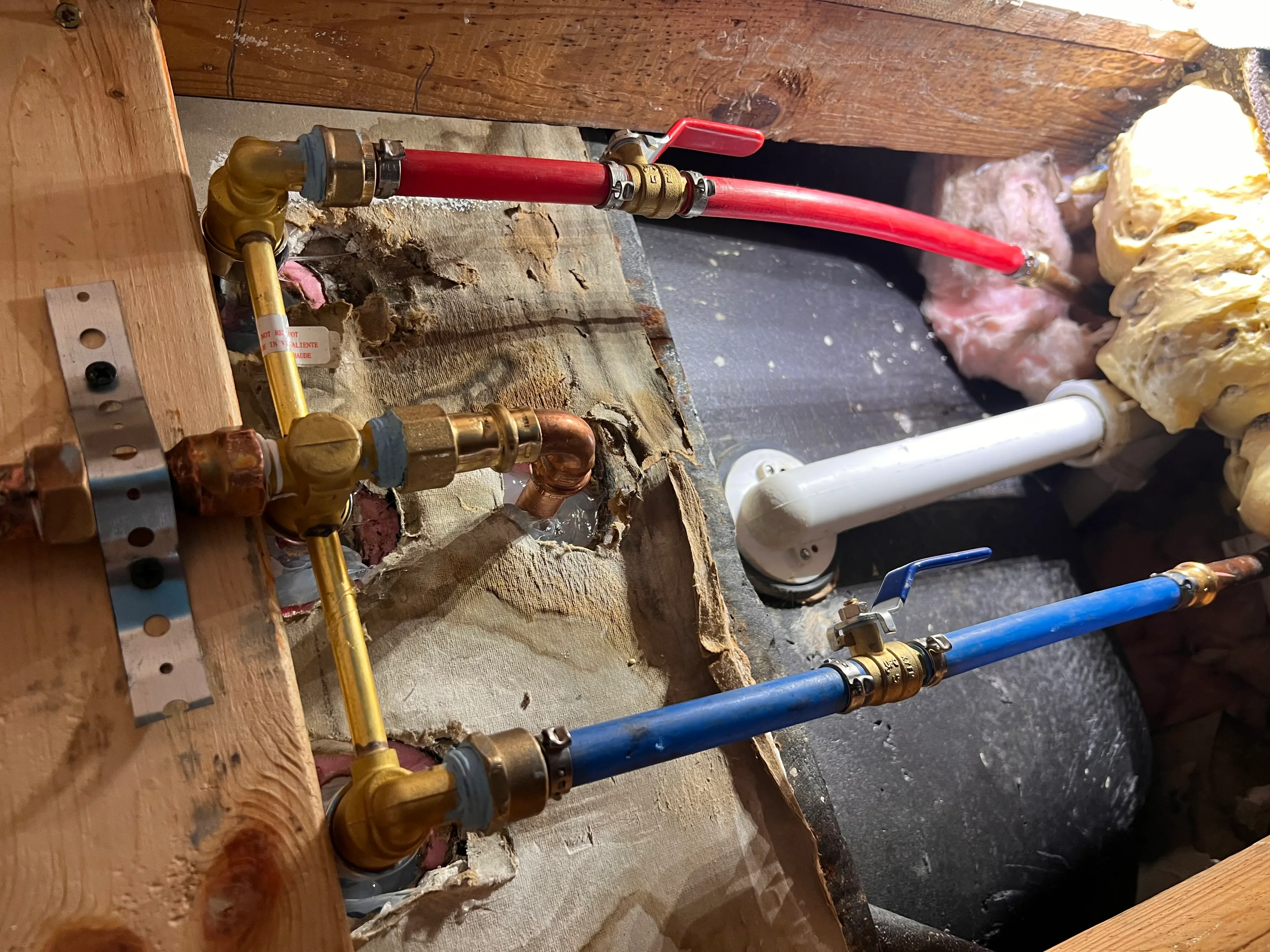 Plumbing rough-in with red, blue, and white PEX/PVC lines, brass fittings, and ball valves on wooden framing