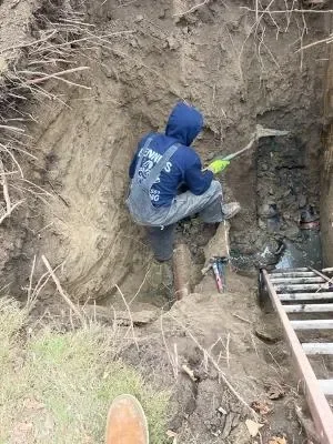 Worker excavating soil to access underground drainage pipe for repair
