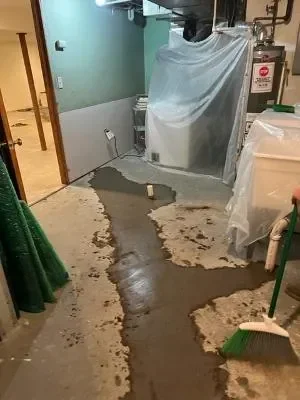 Basement utility room with standing water, wet flooring, and water-damaged materials during emergency plumbing repair