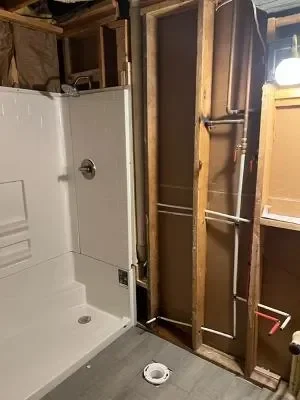 White acrylic shower unit with floor drain and framing studs during installation