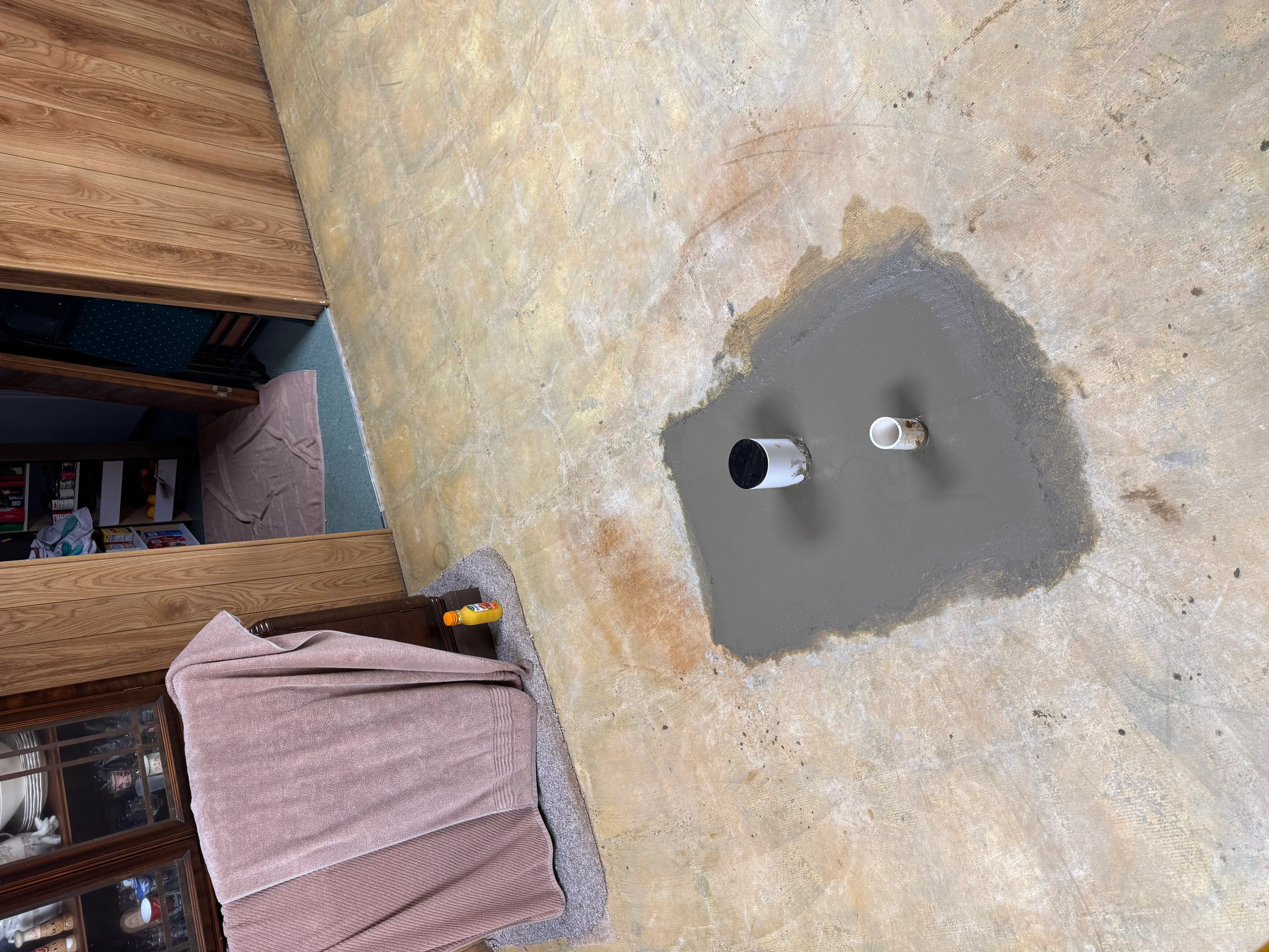 Concrete slab with two PVC pipe rough-in stubs and gray concrete patch for plumbing installation