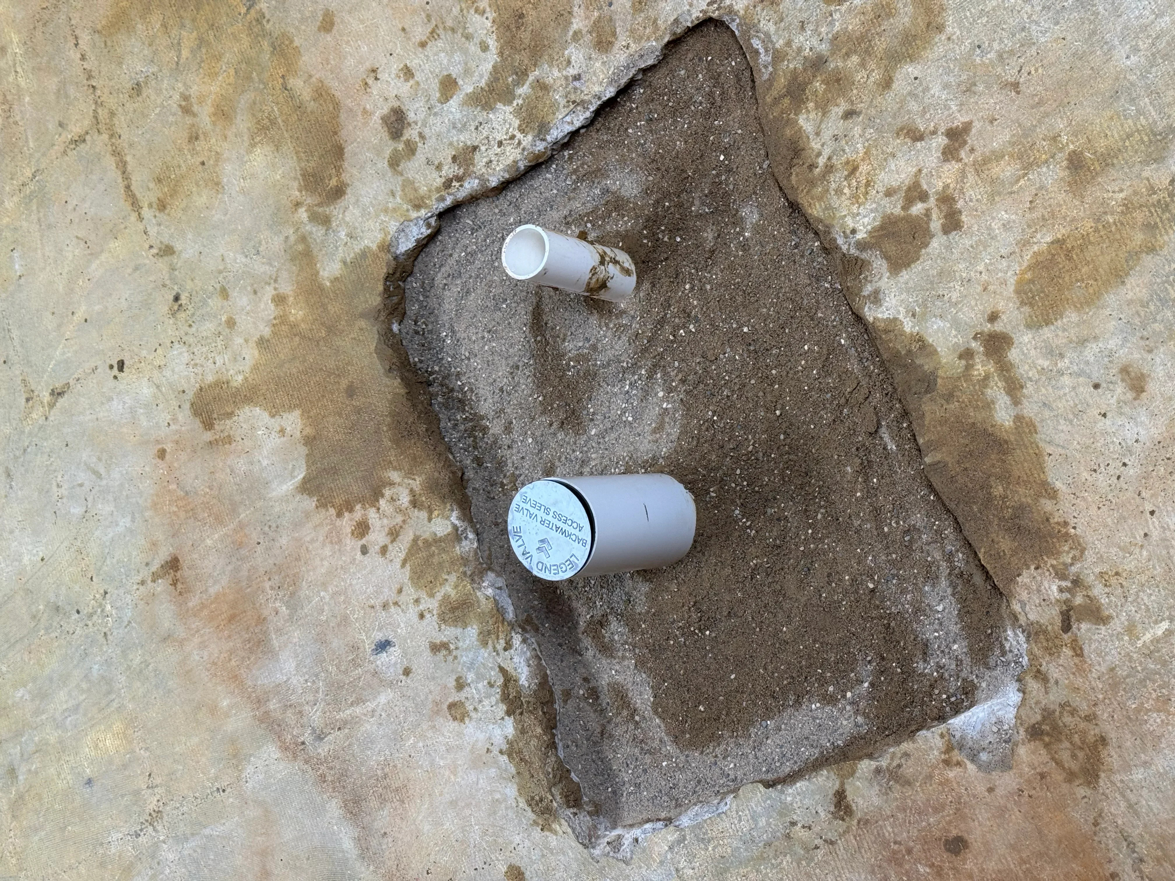 Two white PVC cleanout caps installed in concrete foundation with proper sealing