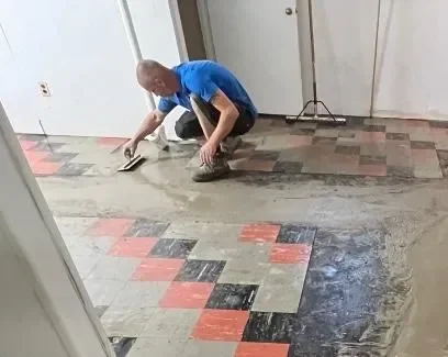 Worker installing geometric patterned tiles on concrete floor with red, black, and gray tiles