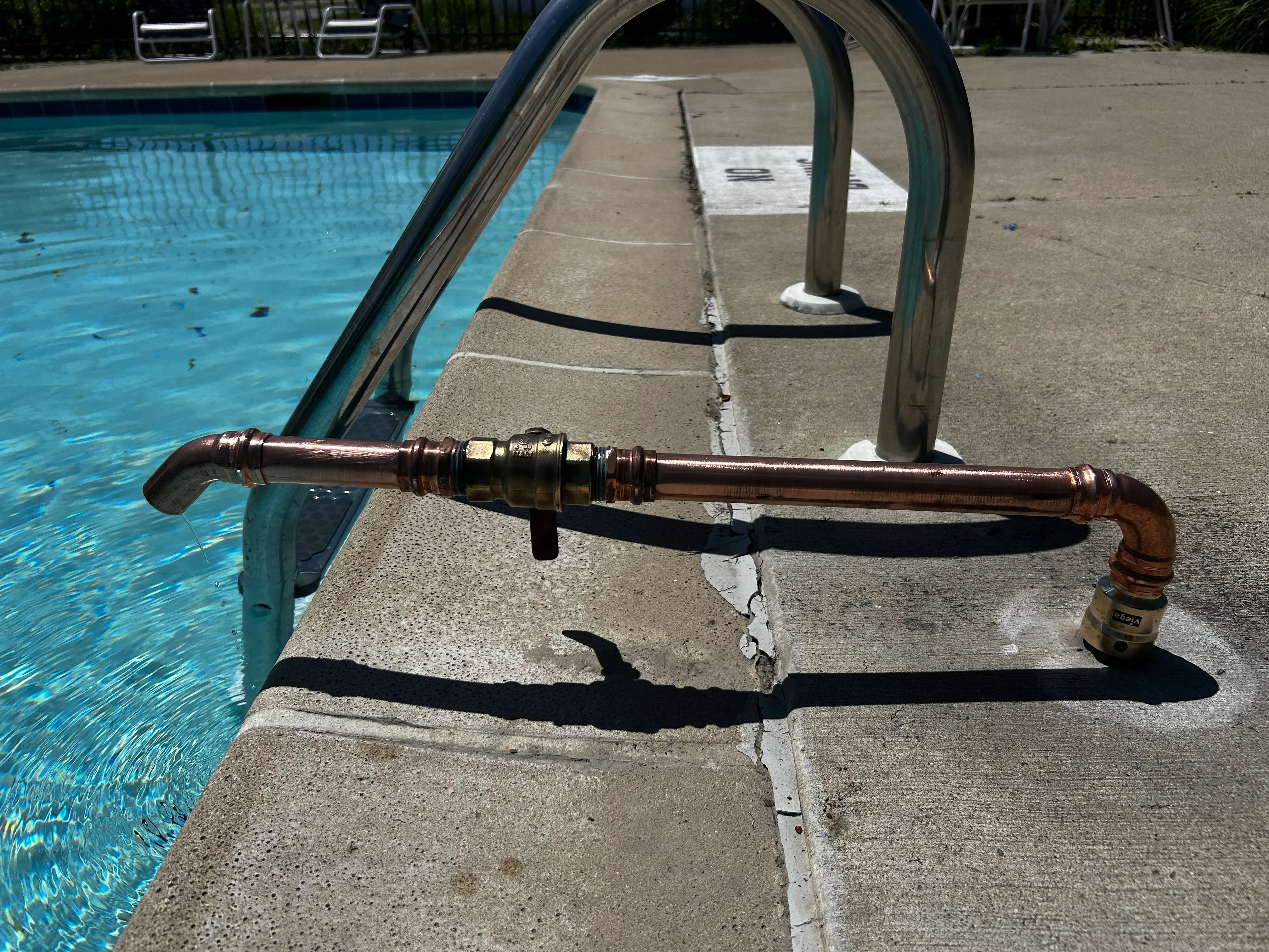 Copper piping with brass fittings and shut-off valve installed at pool deck edge